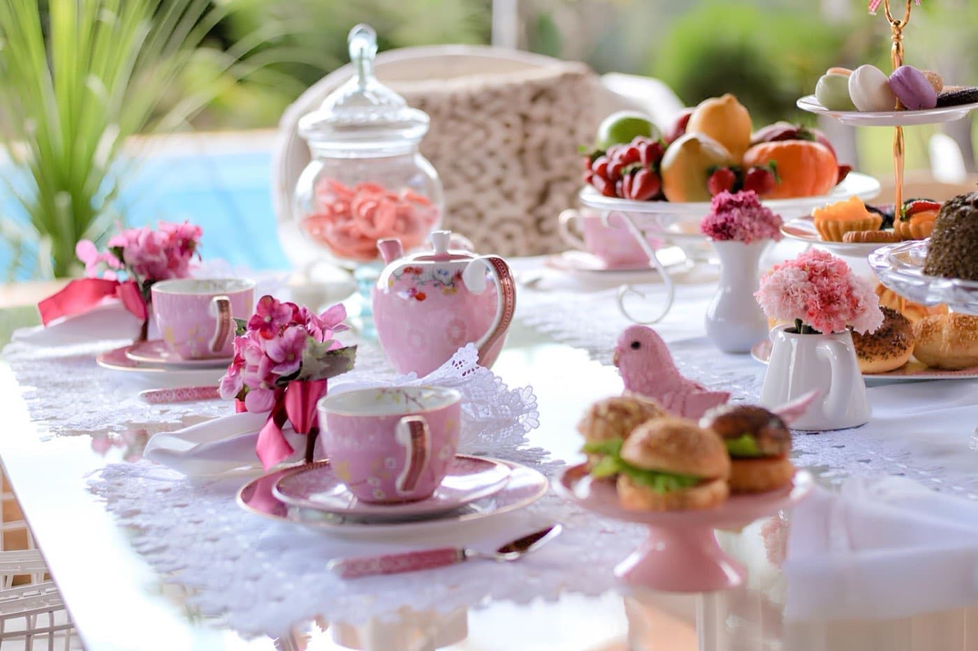 A pink high tea table set with floral teacups, macarons, fruit and finger sandwiches